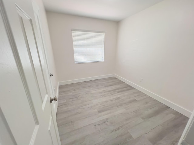 spare room with baseboards and light wood finished floors