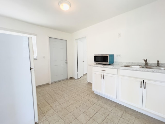 kitchen with light countertops, stainless steel microwave, white cabinetry, a sink, and freestanding refrigerator