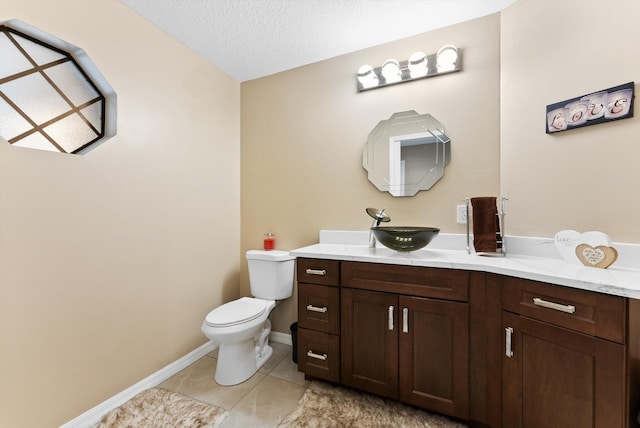 half bathroom featuring vanity, tile patterned floors, toilet, baseboards, and a textured ceiling