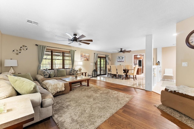 living room featuring visible vents, wood finished floors, and a ceiling fan