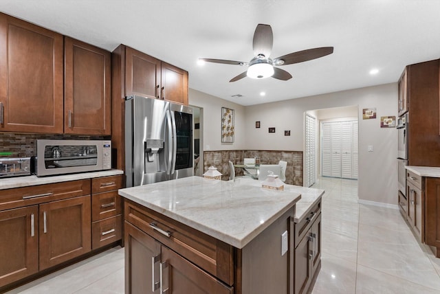 kitchen with decorative backsplash, appliances with stainless steel finishes, a kitchen island, a toaster, and a ceiling fan