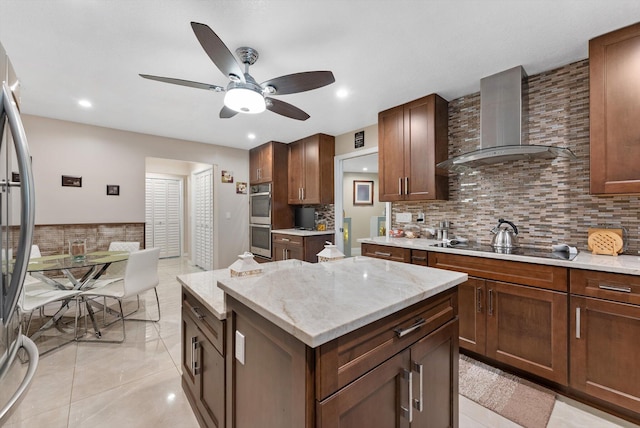 kitchen featuring wall chimney range hood, decorative backsplash, ceiling fan, stainless steel appliances, and a center island