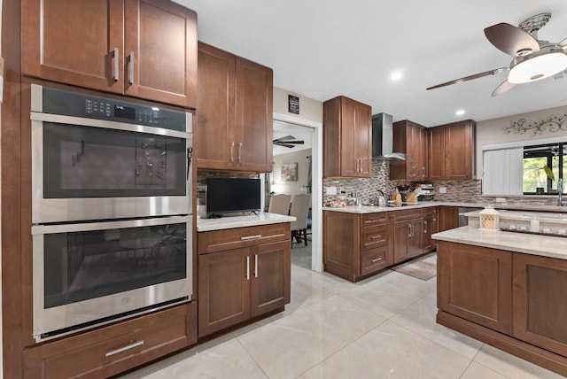 kitchen featuring a ceiling fan, wall chimney exhaust hood, appliances with stainless steel finishes, and decorative backsplash