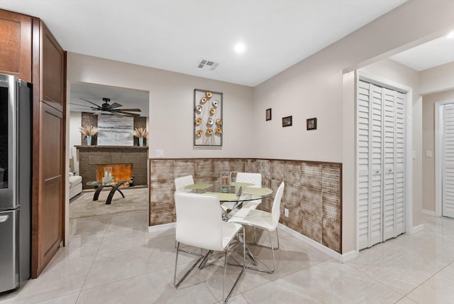dining room featuring visible vents, ceiling fan, a stone fireplace, and baseboards