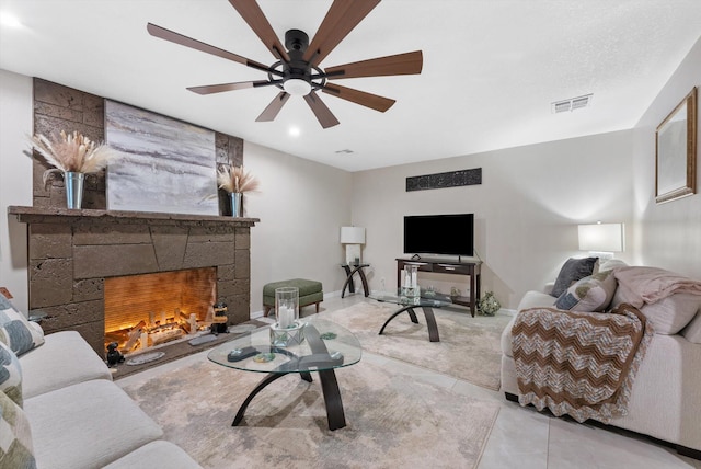 carpeted living area featuring ceiling fan, visible vents, baseboards, tile patterned floors, and a stone fireplace