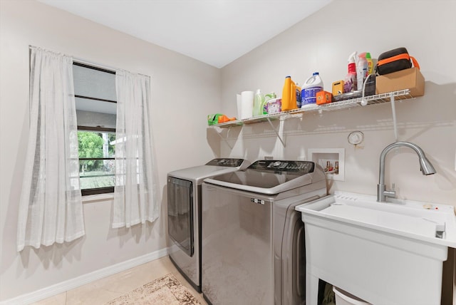 clothes washing area with a sink, baseboards, light tile patterned flooring, washer and dryer, and laundry area