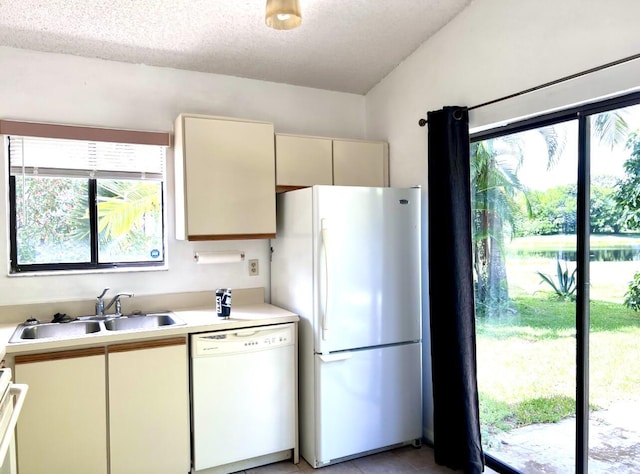kitchen with a sink, light countertops, light tile patterned floors, white appliances, and cream cabinetry