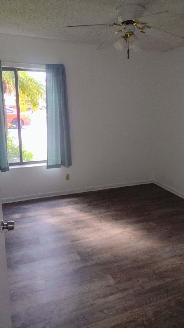 spare room featuring baseboards, ceiling fan, and dark wood-type flooring