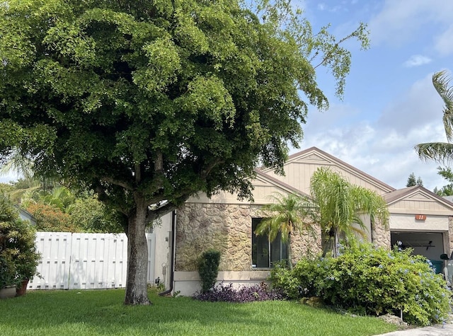 obstructed view of property featuring a front yard, an attached garage, fence, and stone siding