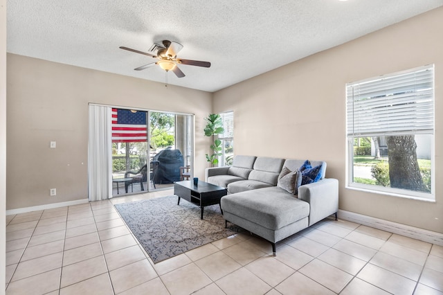 living area featuring a ceiling fan, light tile patterned flooring, baseboards, and a textured ceiling