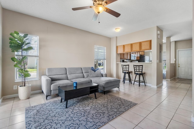 living room with light tile patterned floors, a textured ceiling, baseboards, and ceiling fan