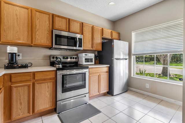 kitchen featuring light countertops, appliances with stainless steel finishes, a textured ceiling, light tile patterned floors, and baseboards