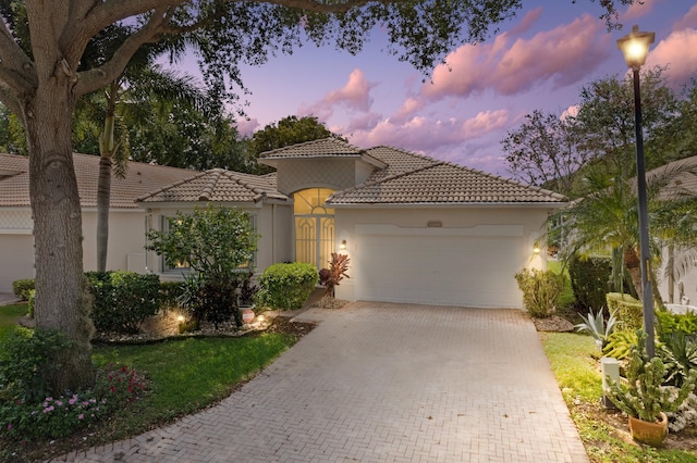mediterranean / spanish-style house with an attached garage, a tile roof, stucco siding, and decorative driveway