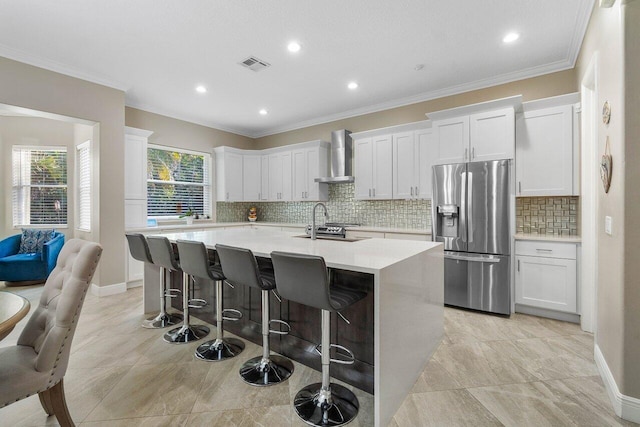 kitchen featuring a kitchen island with sink, tasteful backsplash, visible vents, wall chimney range hood, and stainless steel refrigerator with ice dispenser