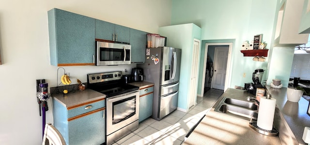 kitchen featuring appliances with stainless steel finishes, light tile patterned floors, a towering ceiling, a sink, and blue cabinets