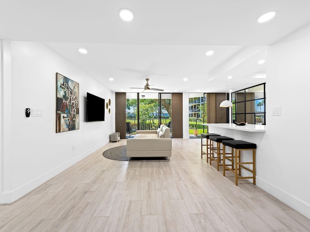 living room featuring baseboards, floor to ceiling windows, recessed lighting, and light wood-style floors