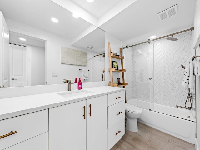 bathroom with toilet, vanity, wood finished floors, visible vents, and shower / bath combination with glass door