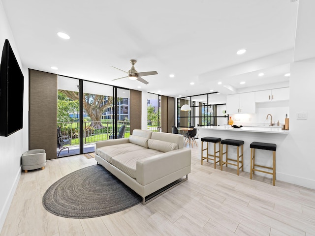 living area featuring a wall of windows, light wood finished floors, baseboards, recessed lighting, and a ceiling fan