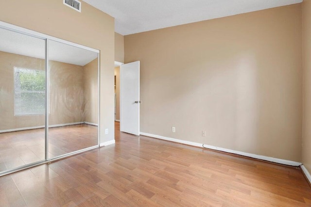 unfurnished bedroom featuring baseboards, visible vents, a closet, and wood finished floors