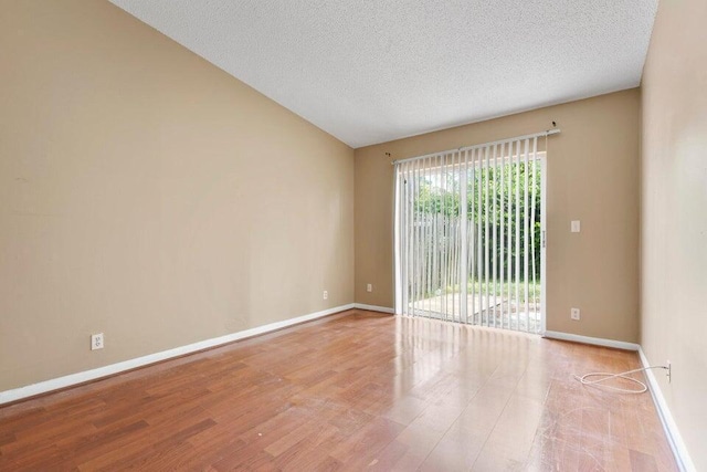 spare room with baseboards, a textured ceiling, wood finished floors, and vaulted ceiling