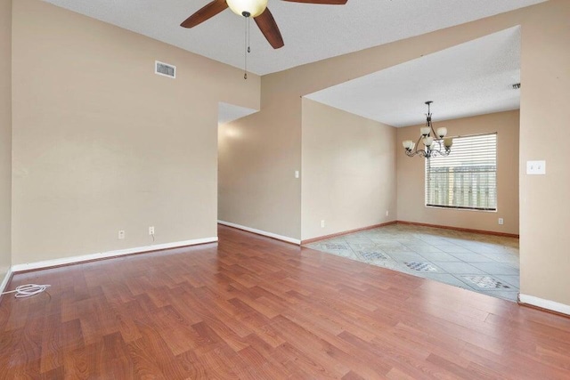empty room featuring ceiling fan with notable chandelier, visible vents, wood finished floors, and baseboards
