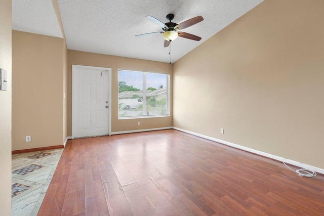 unfurnished room with a textured ceiling, baseboards, wood finished floors, a ceiling fan, and vaulted ceiling