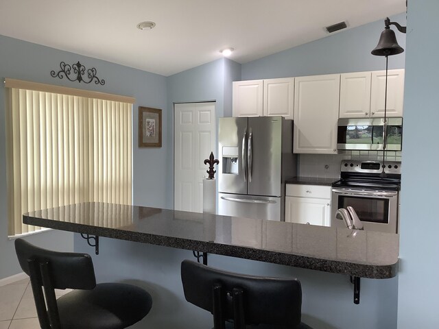 7007 Ashton St, Boynton Beach, FL 33437 - kitchen featuring white cabinets, a breakfast bar area, vaulted ceiling, and stainless steel appliances