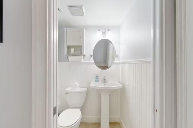 half bathroom featuring a wainscoted wall, visible vents, and toilet