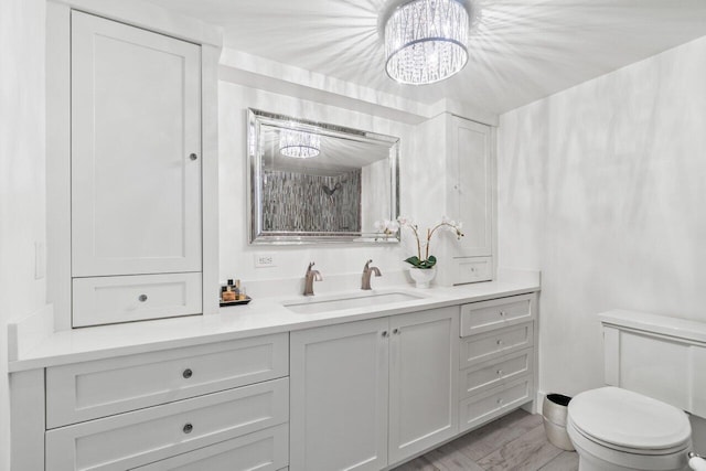bathroom featuring wood finished floors, toilet, vanity, and a chandelier