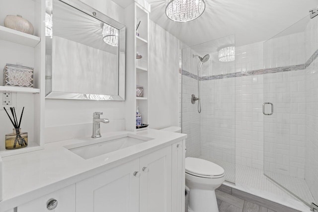 bathroom featuring toilet, vanity, a stall shower, and a chandelier