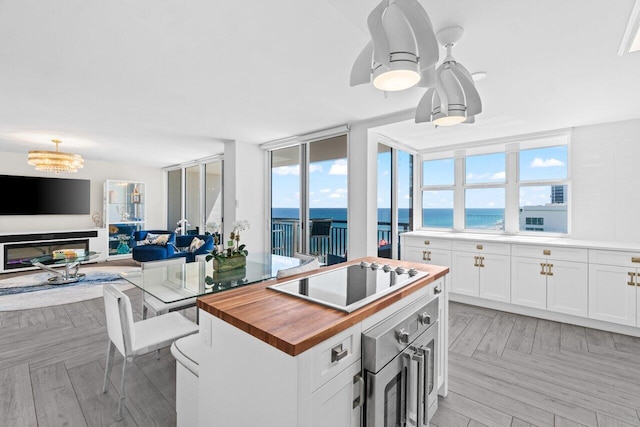 kitchen featuring white cabinets, wooden counters, wall oven, black electric stovetop, and open floor plan