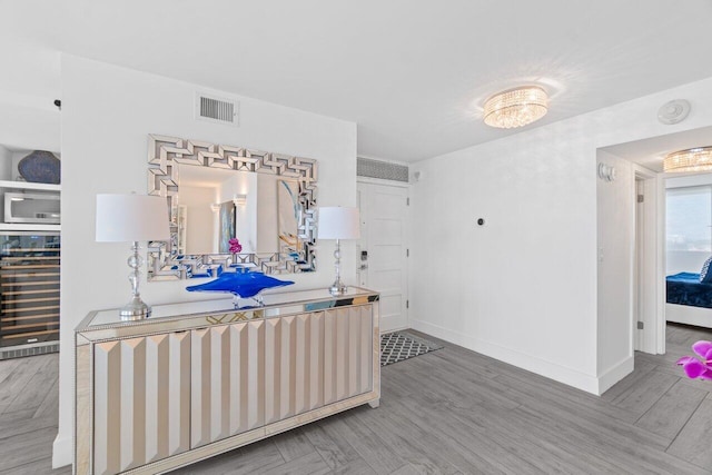 interior space with stainless steel microwave, baseboards, wine cooler, light wood-style floors, and visible vents