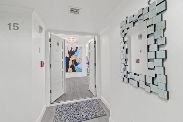 hall with baseboards, visible vents, wood finished floors, and ornamental molding