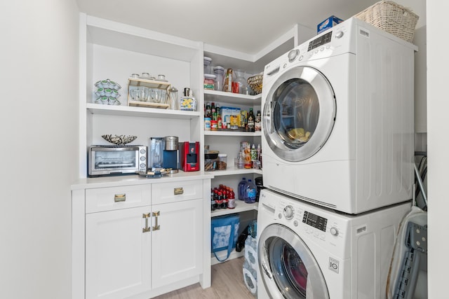laundry room with stacked washer and clothes dryer, cabinet space, and light wood-style flooring