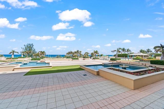 outdoor pool with a patio, a water view, and an in ground hot tub