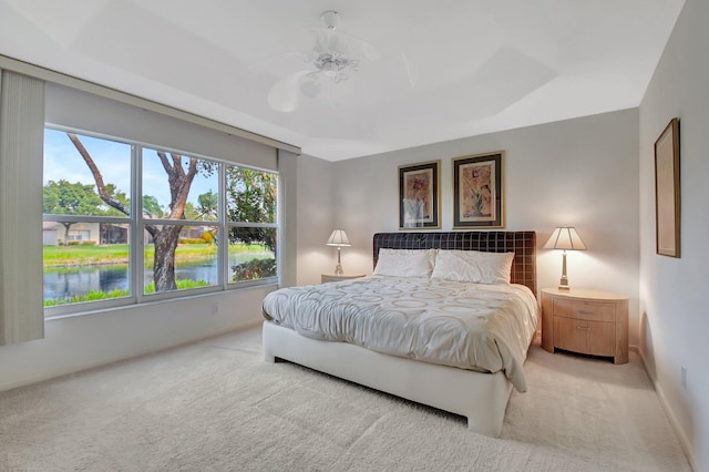 bedroom with a water view, baseboards, light colored carpet, and ceiling fan