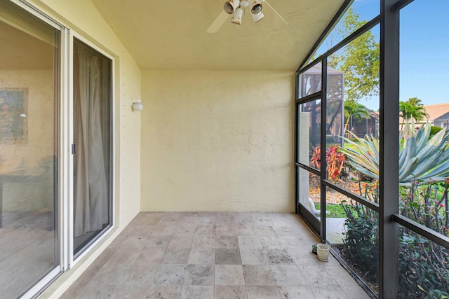 unfurnished sunroom with ceiling fan and a textured wall