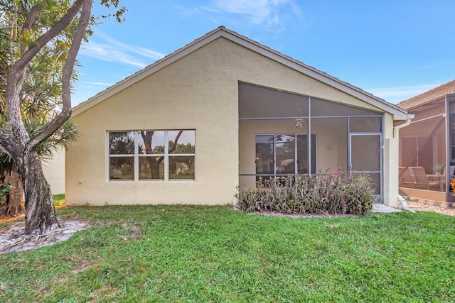 back of property featuring a sunroom, stucco siding, and a lawn