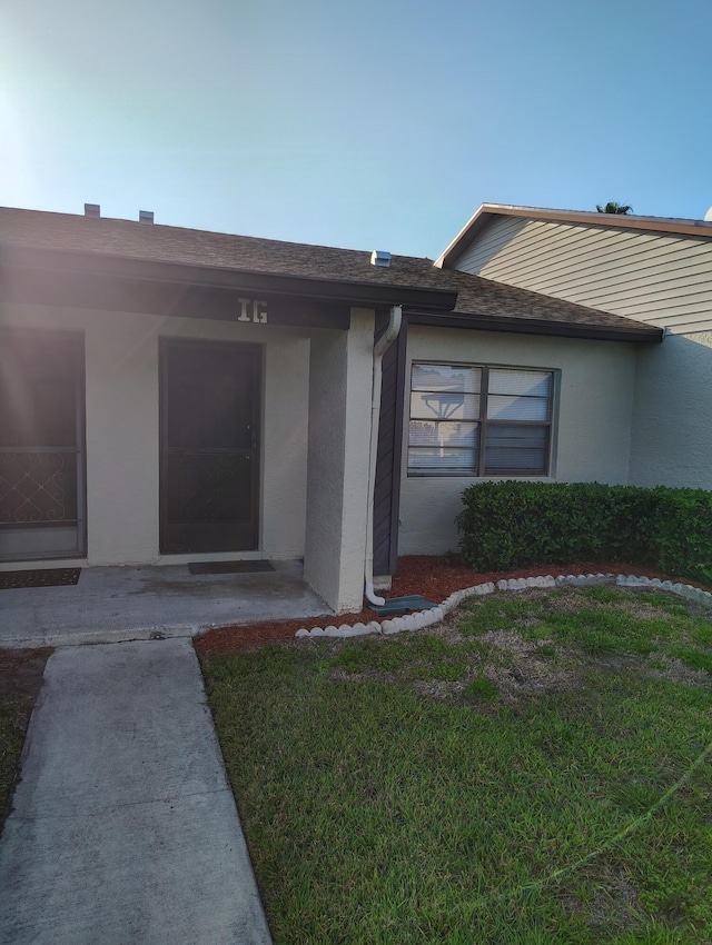 6020 Indrio Rd Unit 6, Fort Pierce, FL 34950 - doorway to property featuring stucco siding, a shingled roof, and a yard