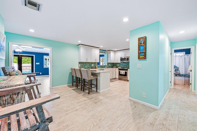 14283 Joan Dr, Palm Beach Gardens, FL 33410 - kitchen featuring appliances with stainless steel finishes, white cabinets, light wood-style flooring, a kitchen breakfast bar, and recessed lighting