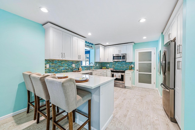 14283 Joan Dr, Palm Beach Gardens, FL 33410 - kitchen featuring stainless steel appliances, a peninsula, light wood-type flooring, tasteful backsplash, and a kitchen bar