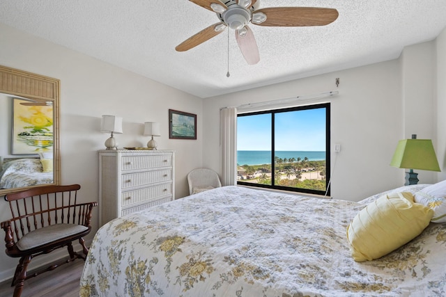 bedroom with a water view, a textured ceiling, wood finished floors, and ceiling fan