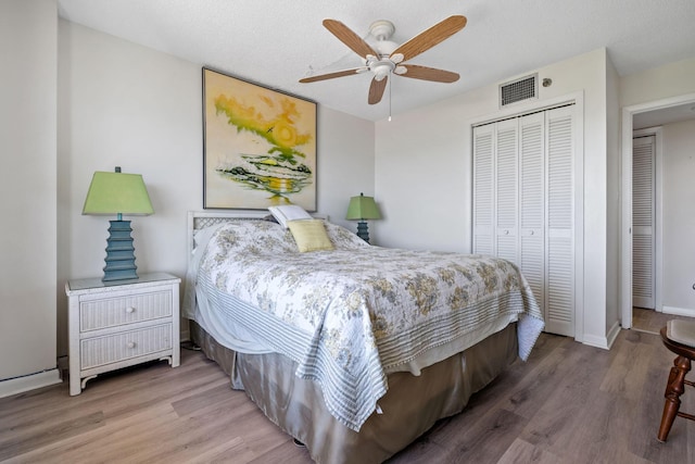 bedroom with wood finished floors, baseboards, a closet, and visible vents