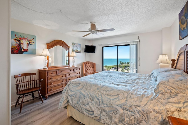 bedroom featuring access to exterior, light wood-style floors, ceiling fan, and a textured ceiling