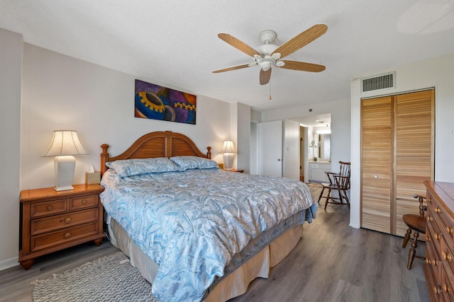bedroom featuring a textured ceiling, ceiling fan, visible vents, a closet, and wood finished floors