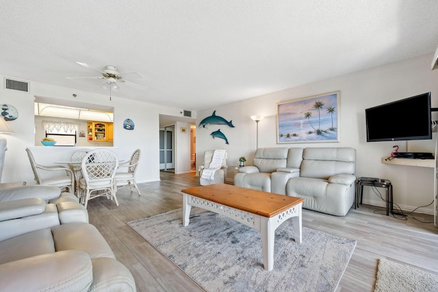 living area featuring a ceiling fan, visible vents, a textured ceiling, and wood finished floors