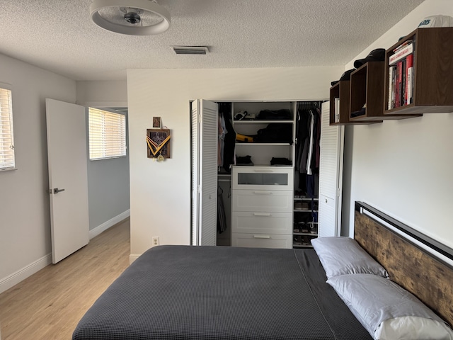 bedroom featuring visible vents, light wood-style floors, a closet, baseboards, and a textured ceiling