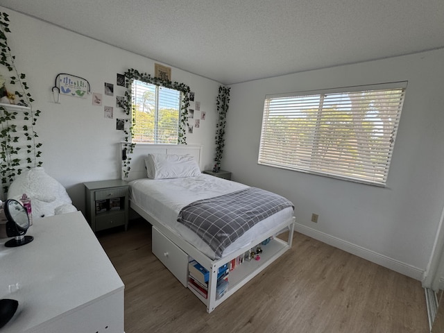 bedroom with baseboards, multiple windows, wood finished floors, and a textured ceiling