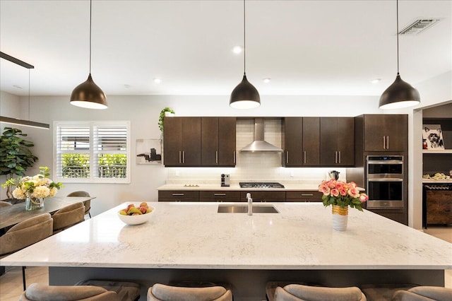 kitchen with visible vents, a kitchen bar, stainless steel appliances, wall chimney exhaust hood, and a sink