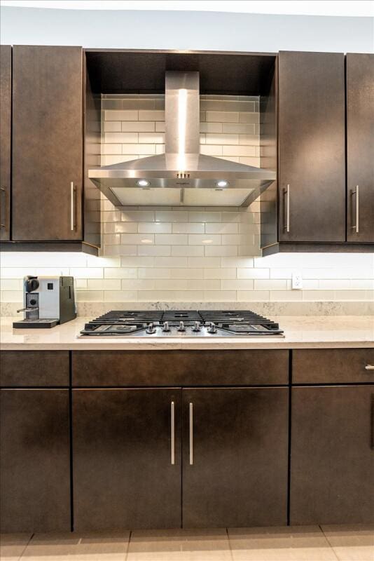 kitchen with dark brown cabinetry, wall chimney range hood, stainless steel gas stovetop, and tasteful backsplash